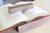 A walnut Bookfellow book rest shown holding the pages down of a book while simultaneously propping it up on a desk.