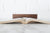 A dark brown wooden book weight shaped like a curved book spine, displayed on top of an open book on a white marble surface against a white brick wall background.