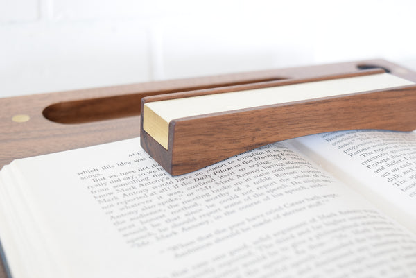 A walnut Bookfellow book rest shown holding the pages down of a book set on a desk.