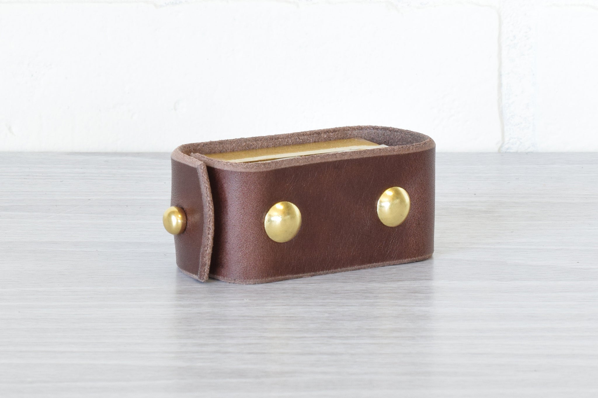 A dark brown Nomad Book Weight shown in the closed position, set on a gray tabletop with white background.