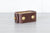 A dark brown Nomad Book Weight shown in the closed position, set on a gray tabletop with white background.