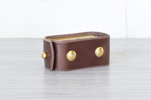 A dark brown Nomad Book Weight shown in the closed position, set on a gray tabletop with white background.