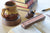 A wooden book weight and pen stand set on an open book, with a ceramic mug, books, and a pen in a softly lit desk scene.