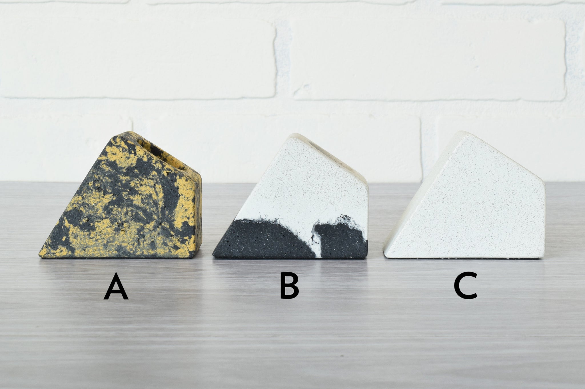 three pen holders, one yellow and black, one white, and one black and white on a gray table with white background