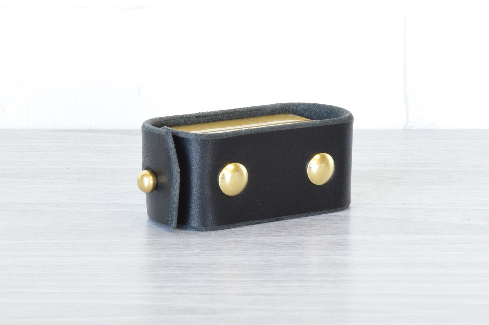 A black Nomad Book Weight shown in the closed position, set on a gray tabletop with white background.
