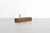 A wooden pen stand with upright brass supports, set on a light gray wooden tabletop against a white brick wall background.
