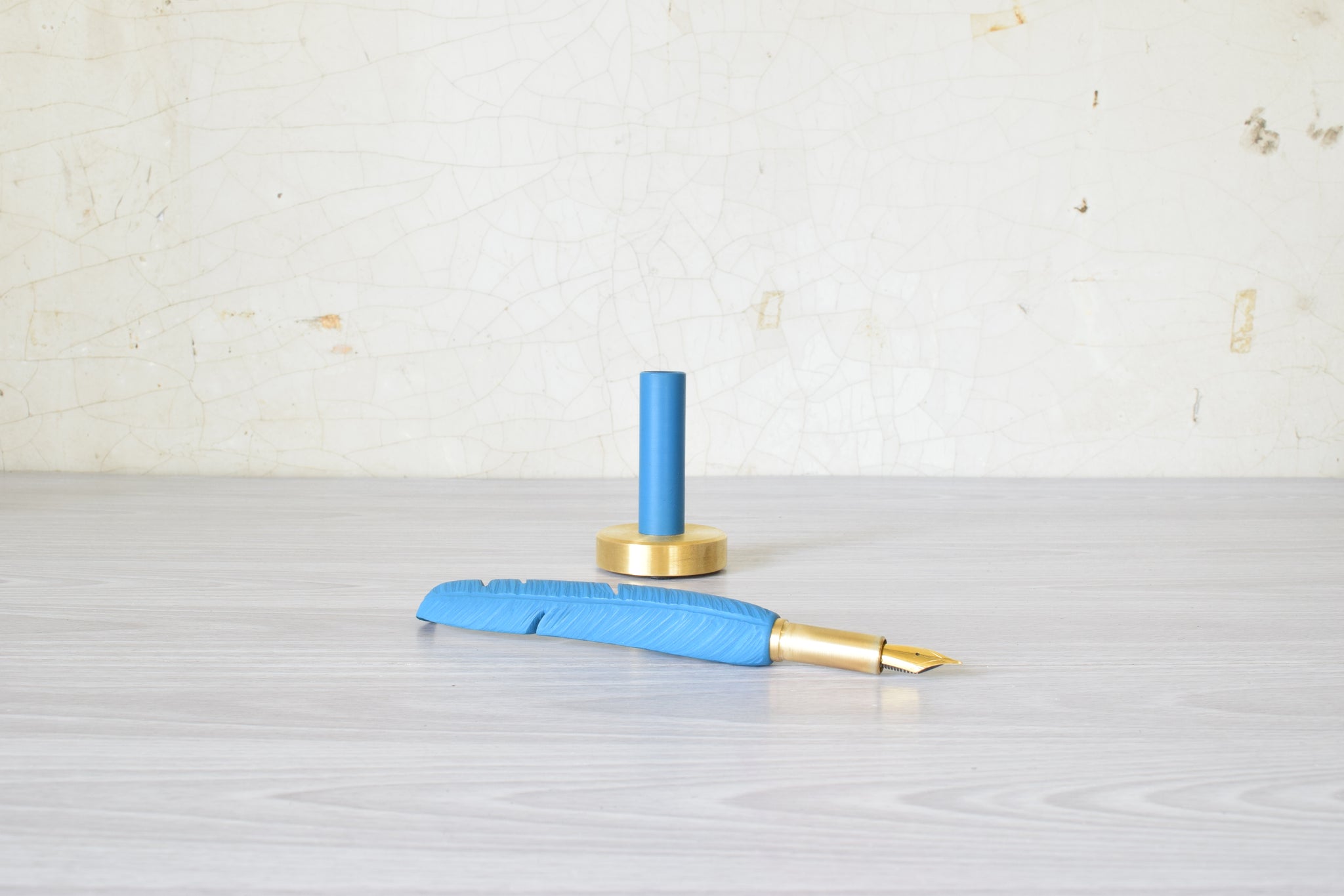 Blue and gold feather pen on a light gray surface with a light beige background