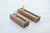 Two rectangular wooden pen stands with a recessed center slot and vertical brass standoffs, shown on a light wood tabletop.