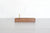 A wooden pen stand with upright brass supports, set on a light gray wooden tabletop against a white brick wall background.
