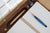 View from above a brown wood lap desk with a notebook, two fountain pens, and a book held open